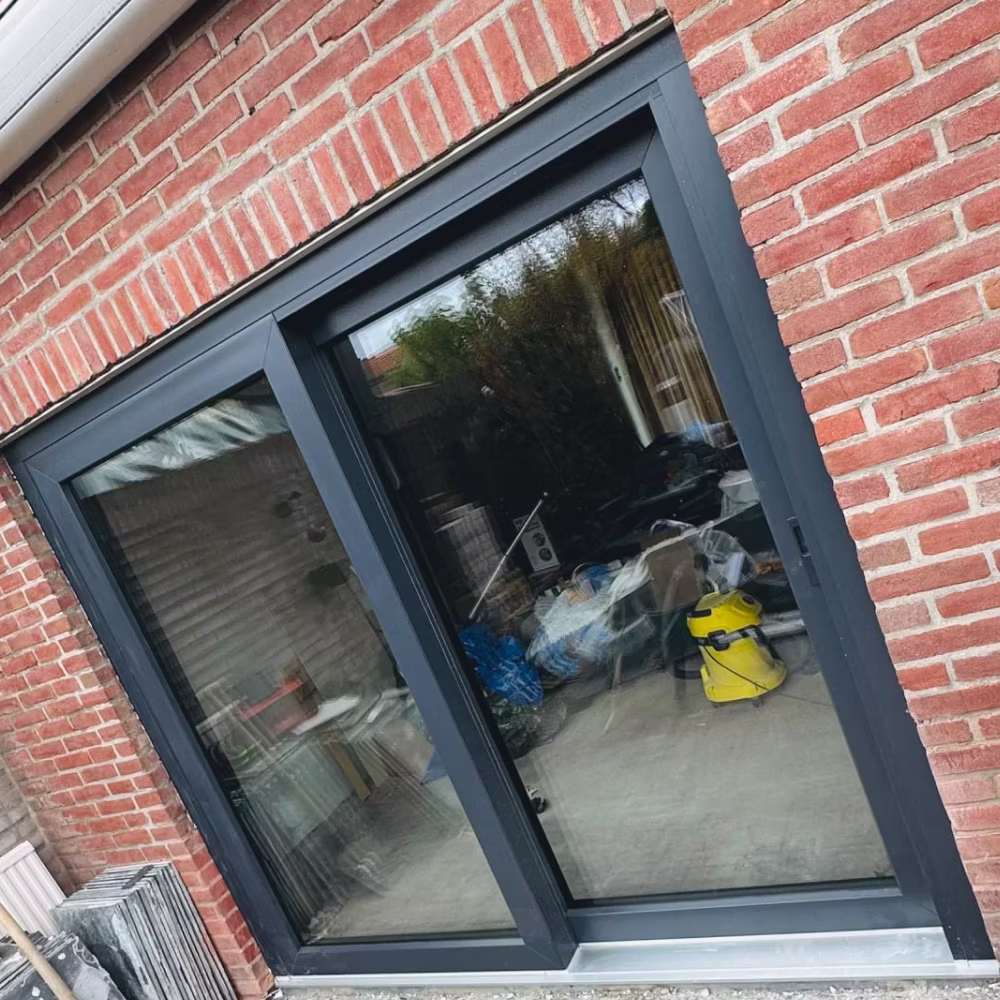 Antracietkleurige schuifpui in een rode bakstenen gevel.