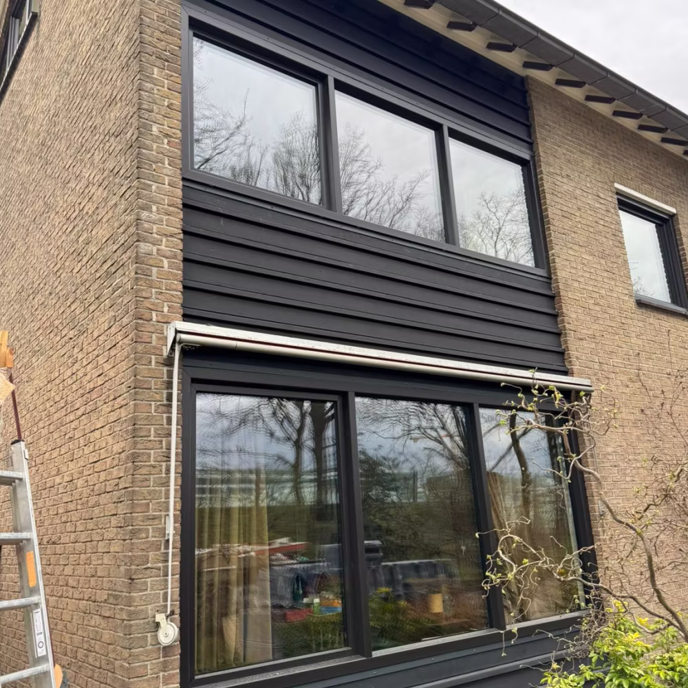 Antracietkleurige kozijnen op twee verdiepingen van een bakstenen woning, met een rolluik.